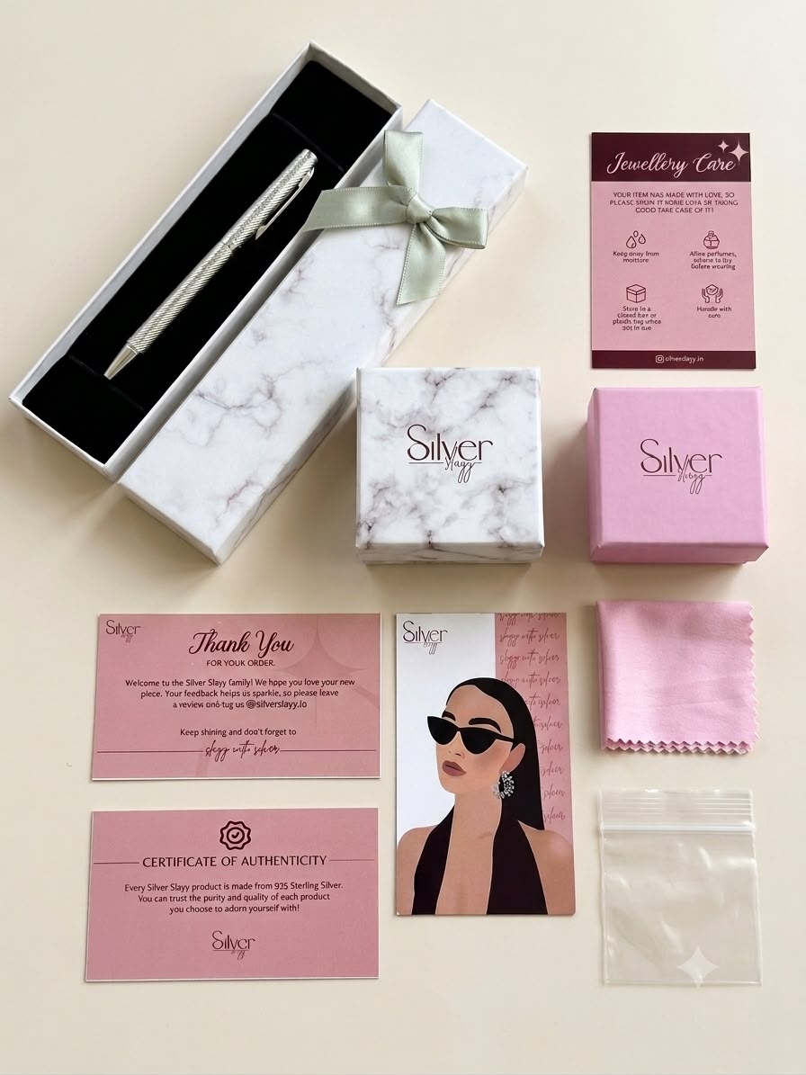 Flat lay of a 925 sterling silver pen inside a marble gift box with authenticity certificate and care clot.