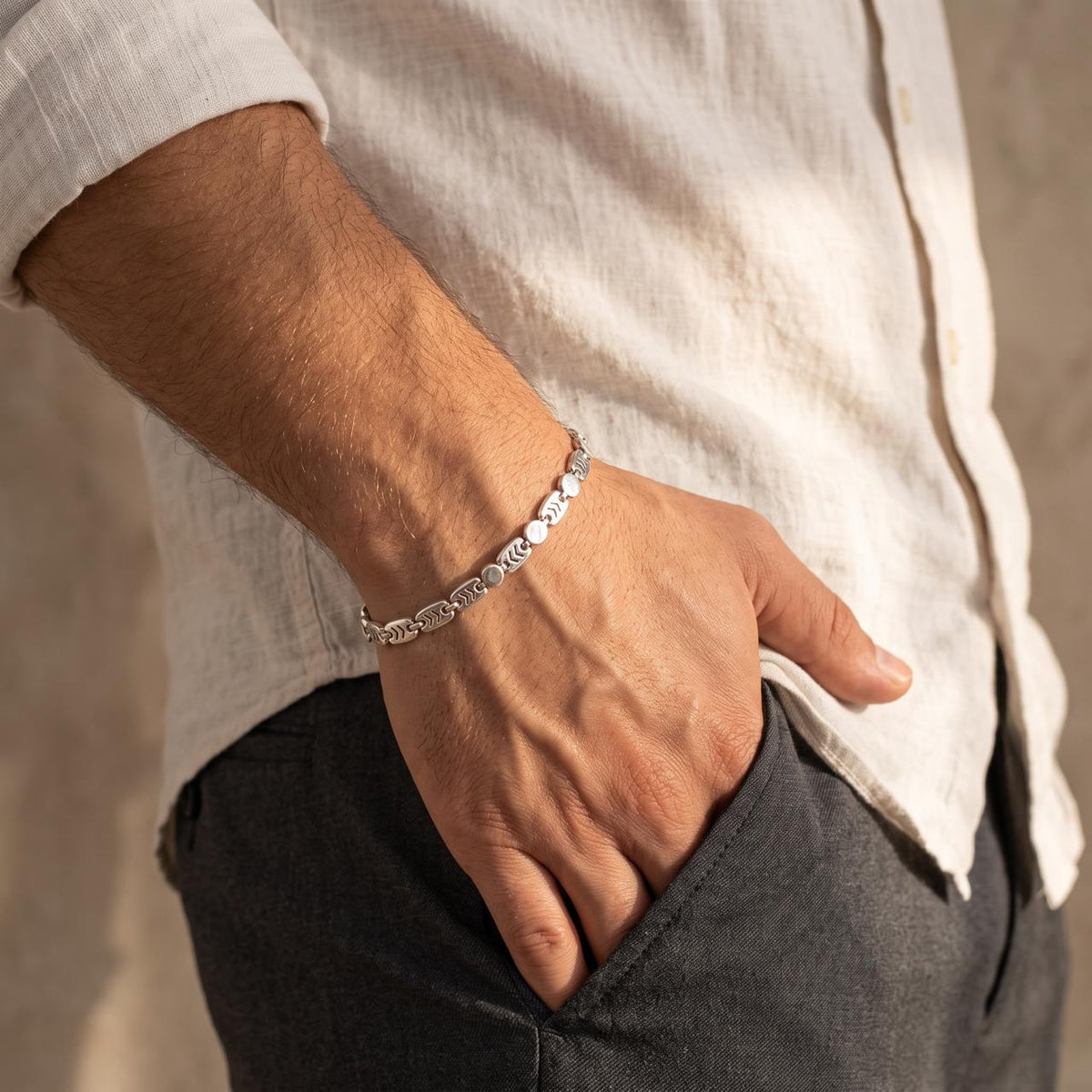 Side angle of a male wrist wearing a 925 sterling silver bracelet with alternating chevron-carved and round disc links.
