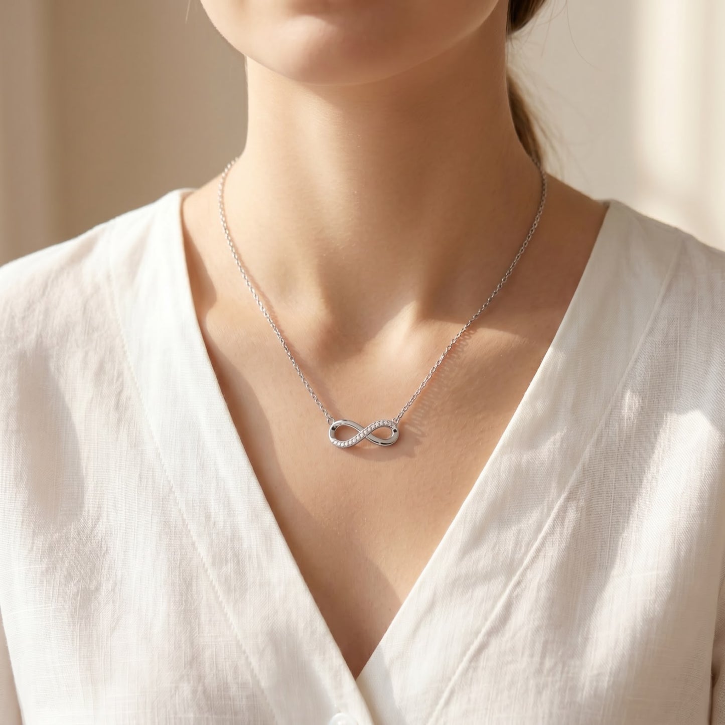 Front close-up view of a 925 silver chain featuring a stone-studded infinity loop pendant worn on a woman's neckline.