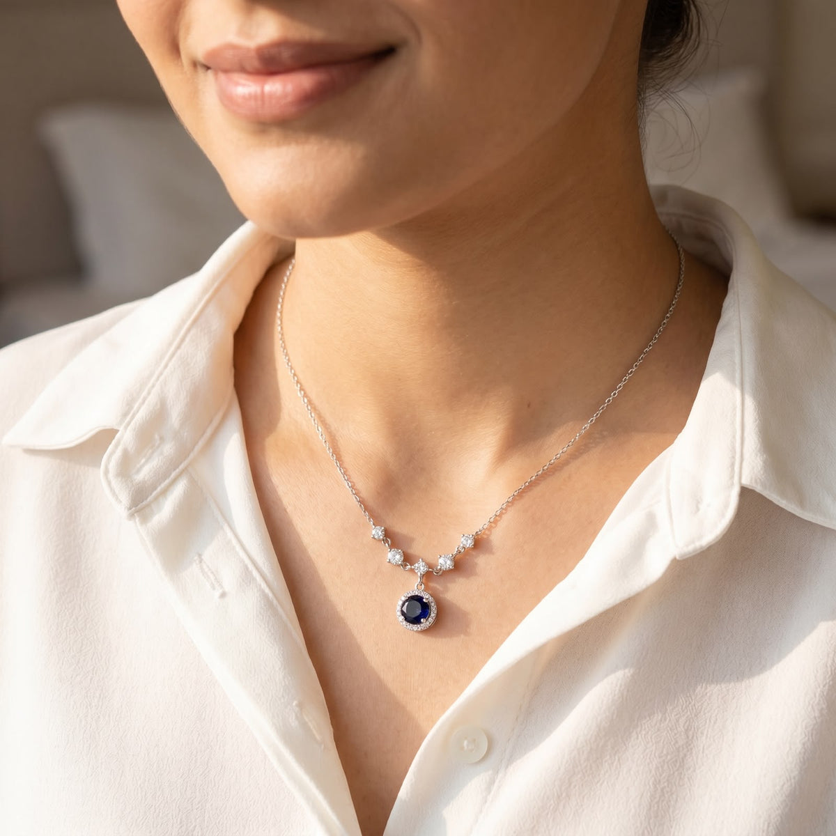 Front view of a 925 silver chain necklace featuring a circular blue stone halo pendant, worn on a woman's neckline over a white button-down shirt.