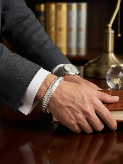 Close-up of a men's textured silver kada cuff bracelet with a diagonal carved pattern, worn on a wrist styled with a formal grey suit.