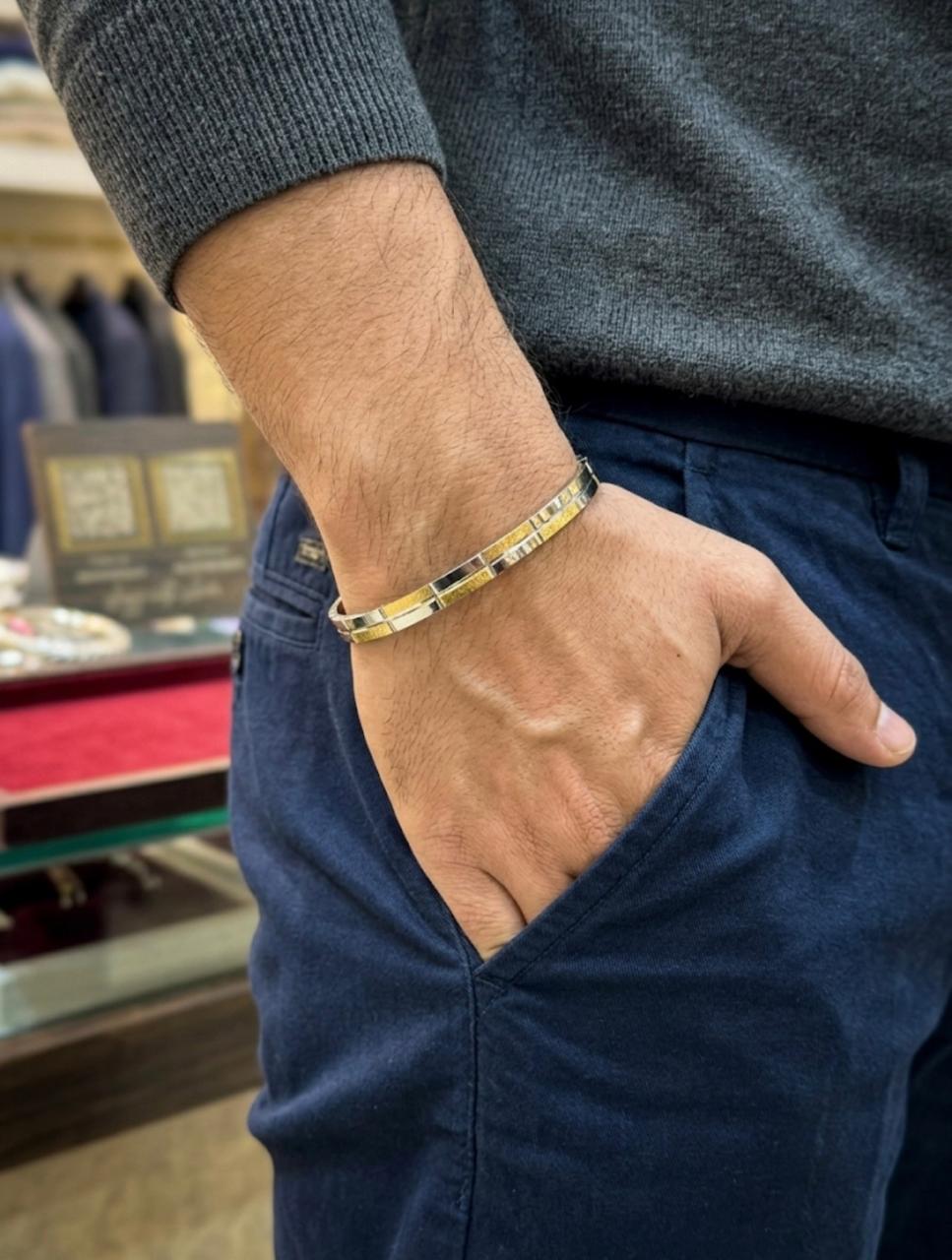 Close-up of a men's dual-tone silver kada cuff bracelet with textured gold-tone accents, worn on a wrist styled with casual menswear.