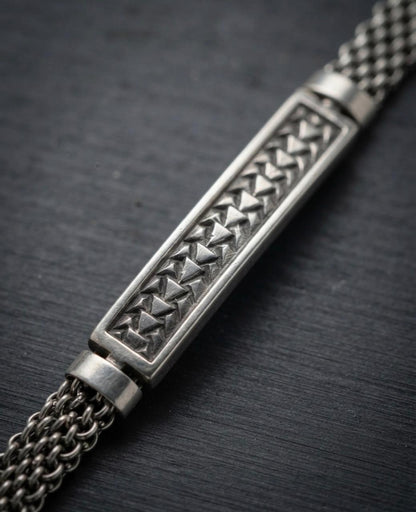 Macro close-up of a 925 sterling silver bracelet showing a rectangular bar with embossed triangle motifs and woven mesh chain.