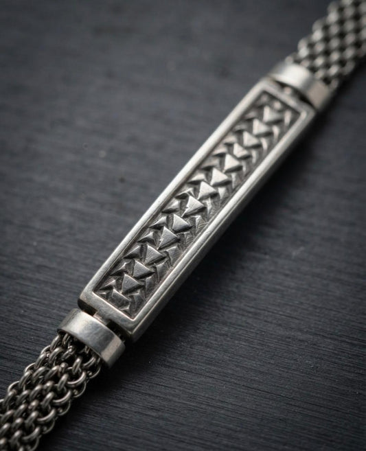 Macro close-up of a 925 sterling silver bracelet showing a rectangular bar with embossed triangle motifs and woven mesh chain.