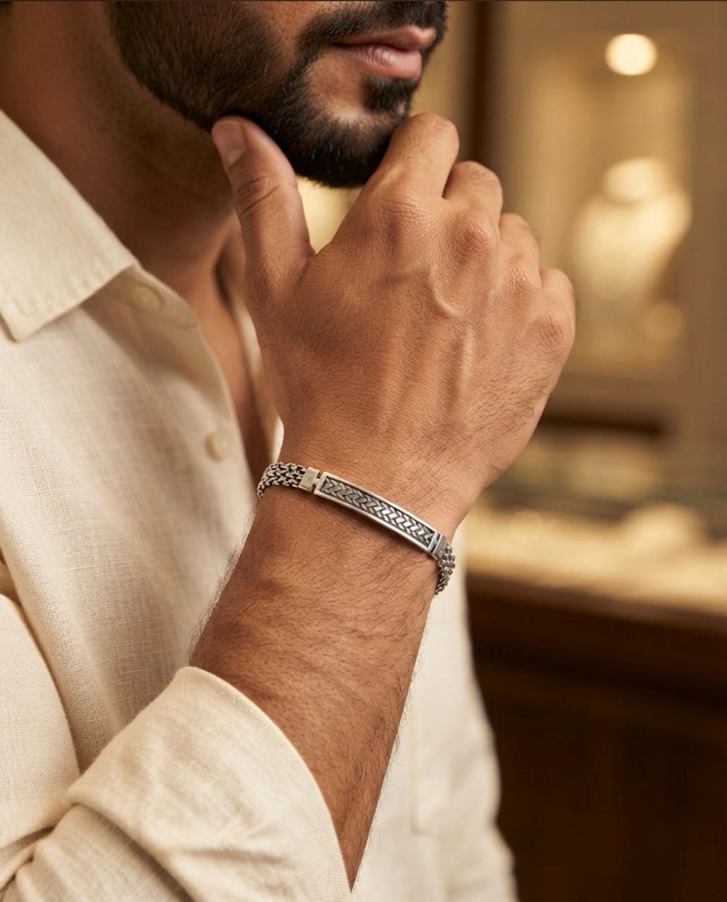 Close-up of a 925 sterling silver bracelet with a braided chain and engraved centre bar worn on a man's wrist with a beige shirt.