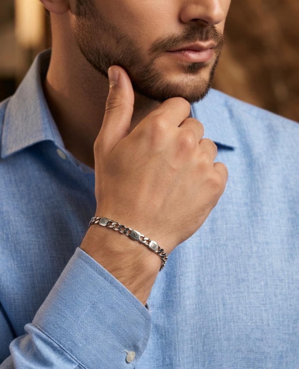 Close-up of a man wearing a 925 sterling silver bracelet with Greek key accent links and polished chain connectors, paired with a light blue shirt.