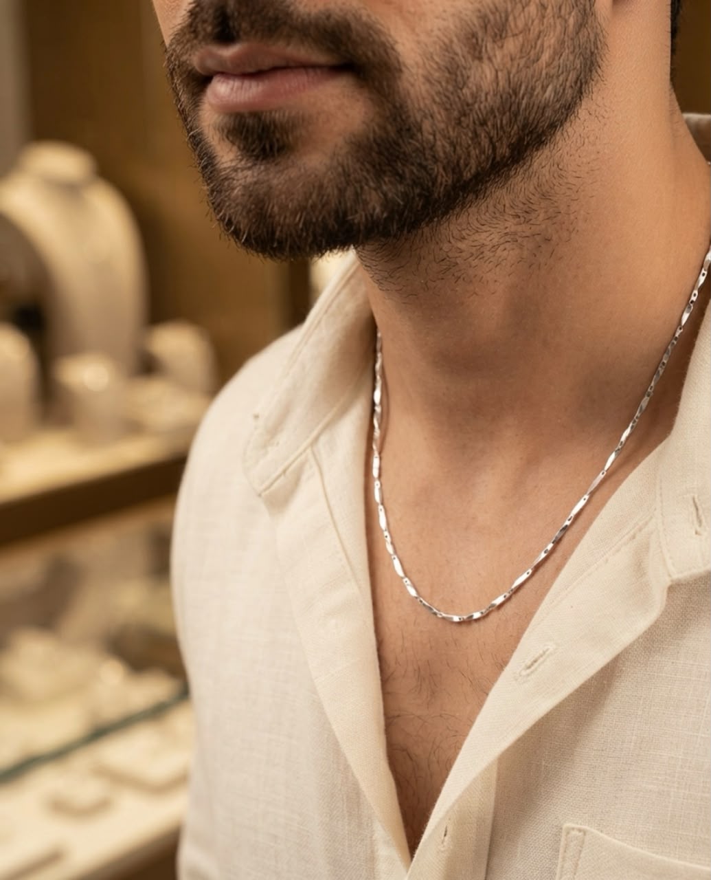 Close-up of a man wearing a 925 sterling silver faceted link chain with a slim polished design over an open-collar cream shirt.