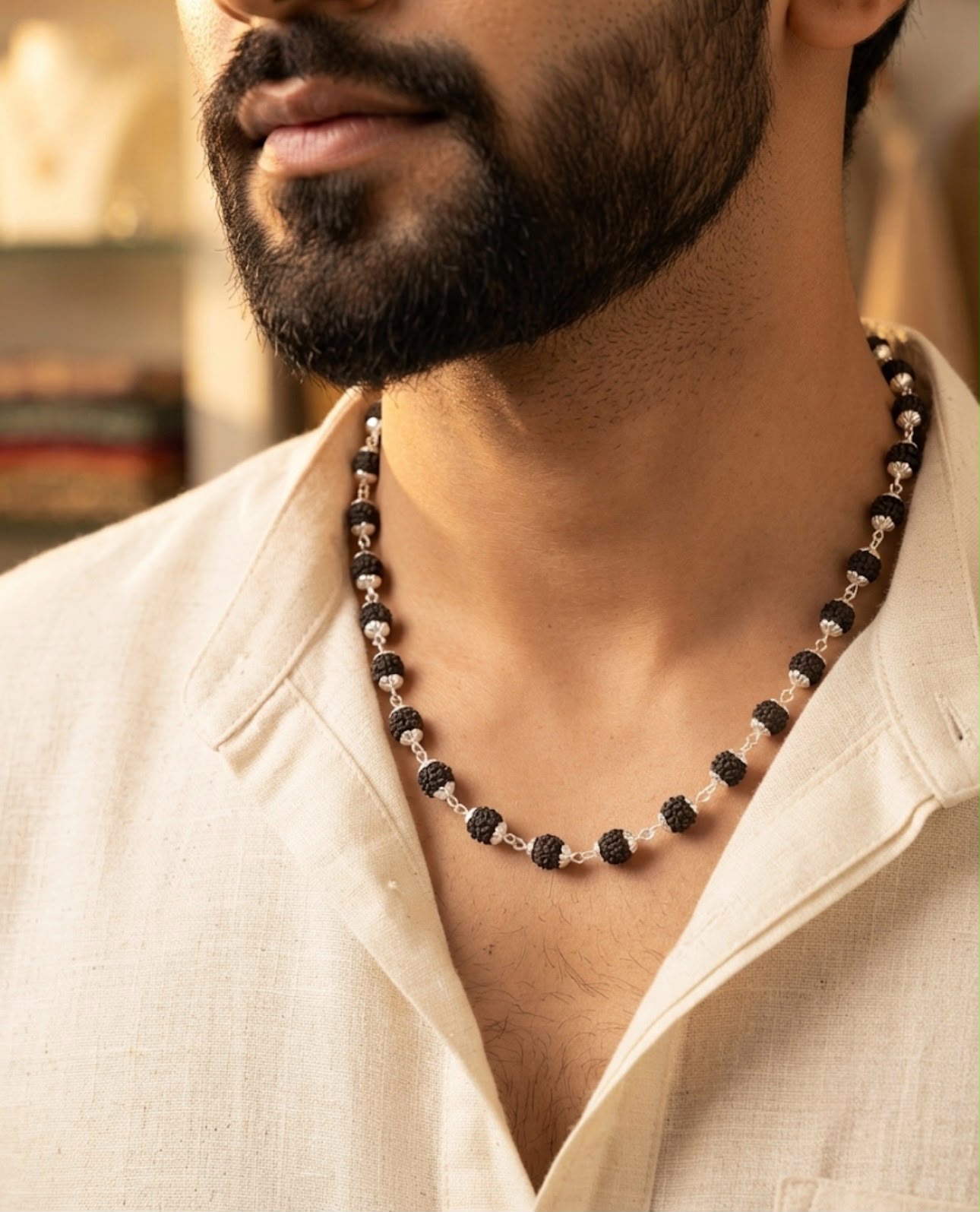 Close-up of a man wearing a 925 sterling silver Rudraksh chain with black textured Rudraksh beads and silver links over an open-collar cream shirt.