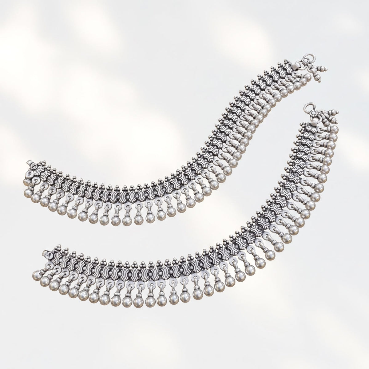 Overhead flat lay of 92% purity oxidised silver heavy payal pair showing carved link texture and bead fringe on light background.