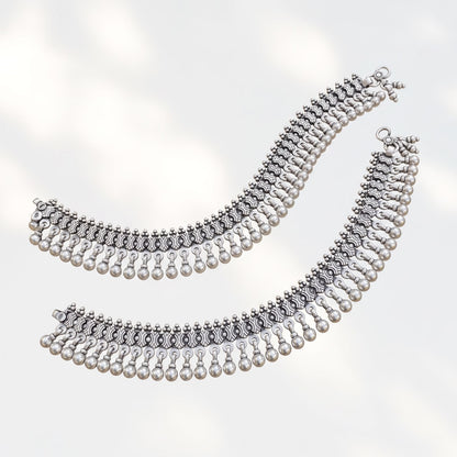 Overhead flat lay of 92% purity oxidised silver heavy payal pair showing carved link texture and bead fringe on light background.