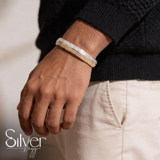 Man wearing a 925 sterling silver bracelet for him with a Greek key border pattern and layered linear detailing on the wrist.