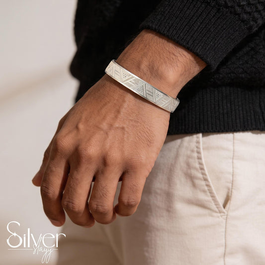 Close-up side view of a man wearing a 65% purity silver bracelet with repeating geometric and triangular engraved patterns.