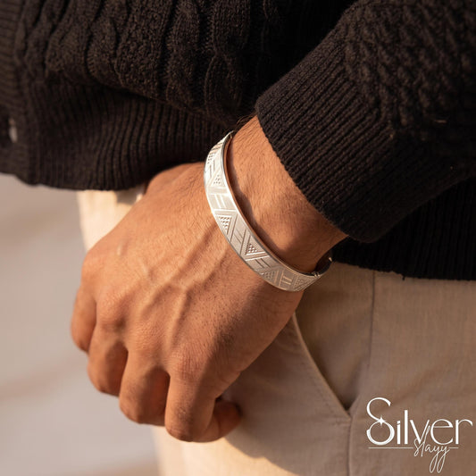 Man wearing a 65% purity silver bracelet with engraved triangular geometric panels and diagonal detailing on his wrist.
