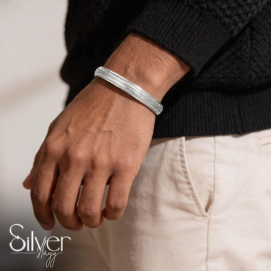 Man wearing a 65% purity silver bracelet with triple-line borders and fine textured detailing on his wrist.