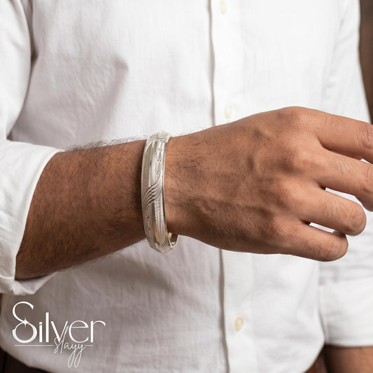 Man wearing a 925 purity silver bracelet with flowing wave engravings, fine vertical lines, and circular accents on his wrist.