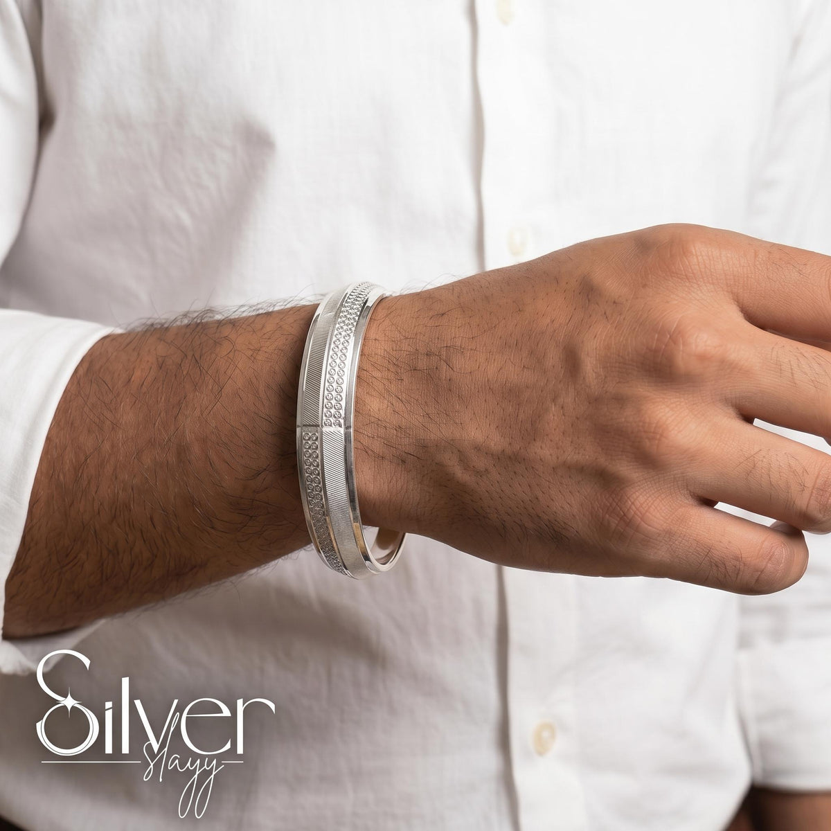 Man wearing a 925 purity silver bracelet with circular textured accents and fine linear detailing on his wrist, styled with a white shirt.