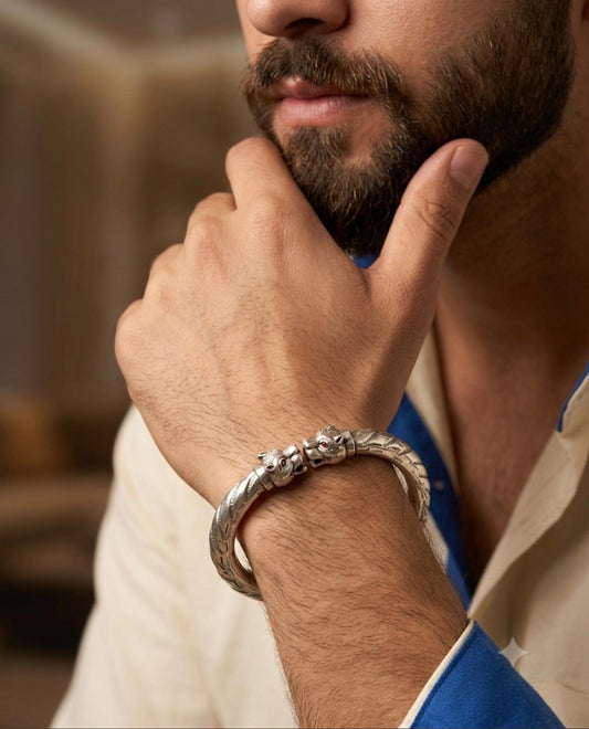 925 silver men's kada with twin lion head motifs and textured engraved band, worn on a wrist with a blue and white outfit.